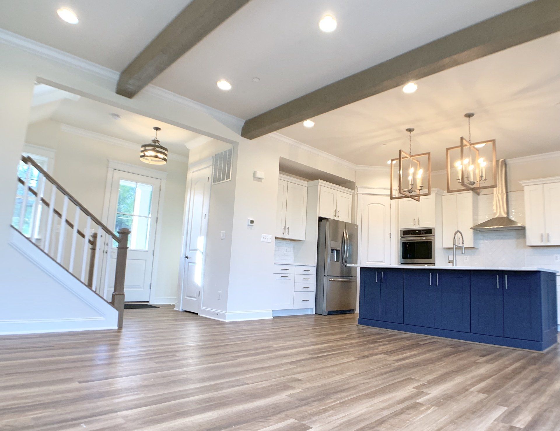 Open-concept kitchen with white cabinets, blue island, stainless steel appliances, and wooden beams.