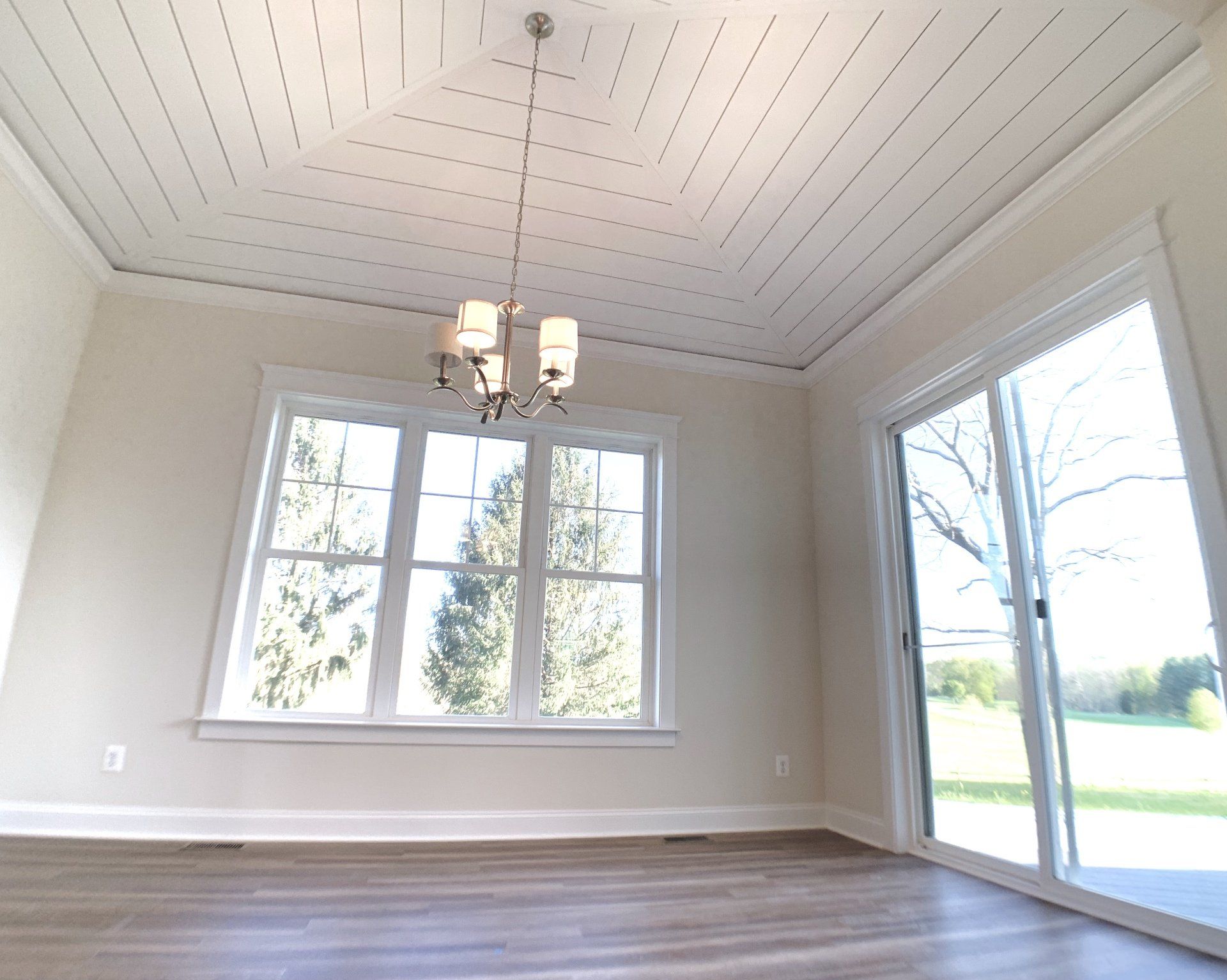 Empty room with wood flooring, white walls, windows, and a chandelier.