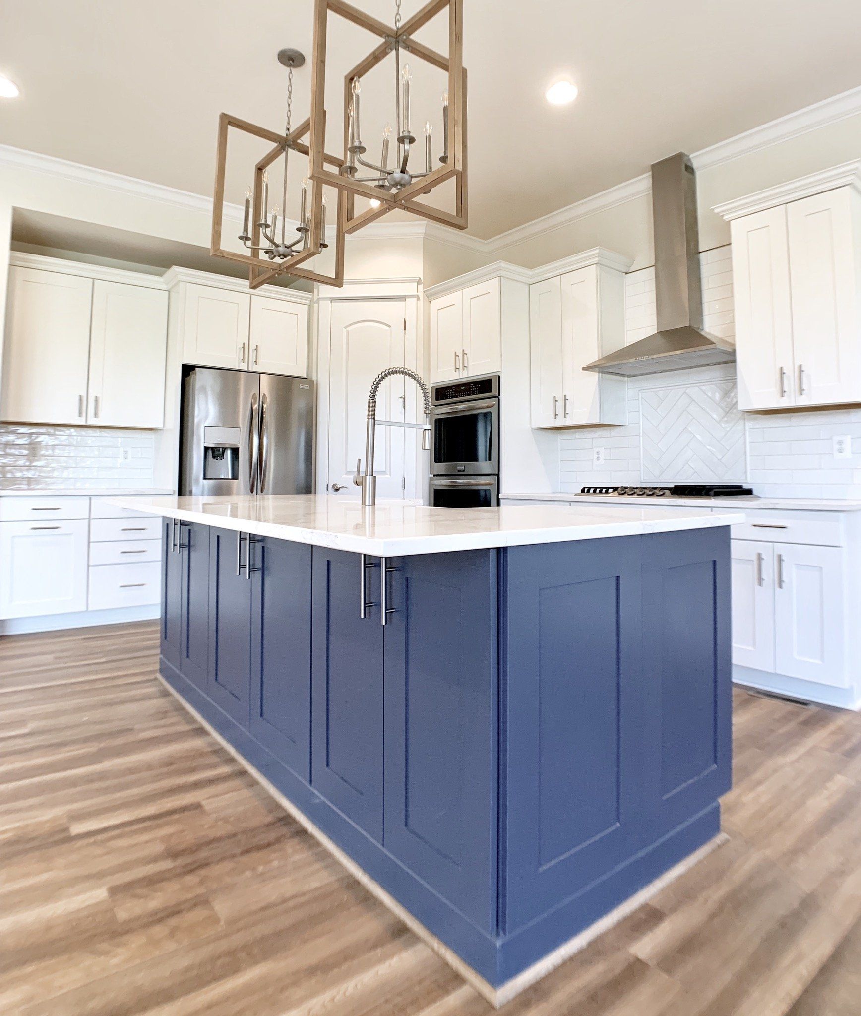 Blue kitchen island with white countertop, white cabinets, stainless steel appliances, and light wood floors.
