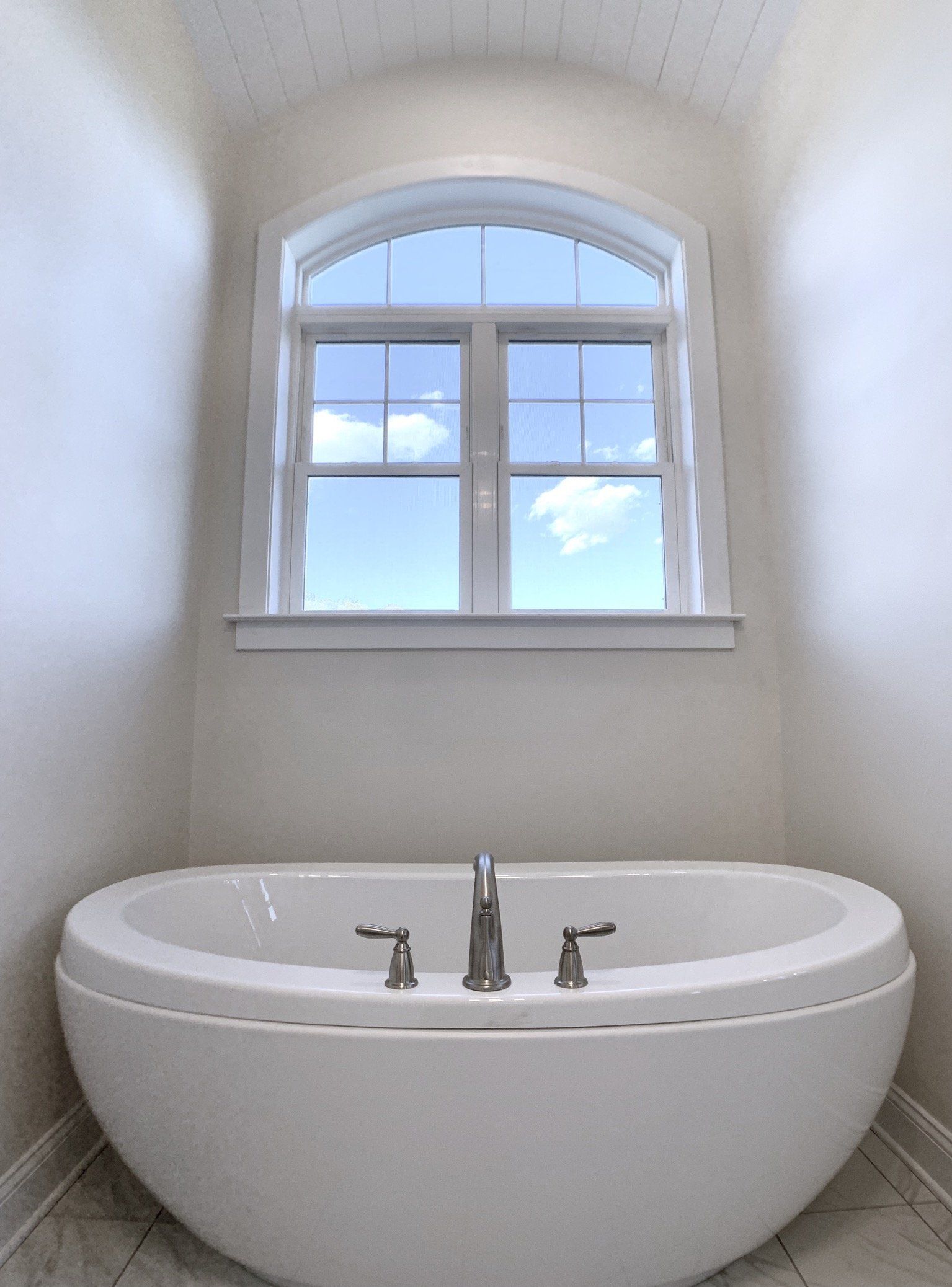 White oval bathtub under arched window, blue sky visible.