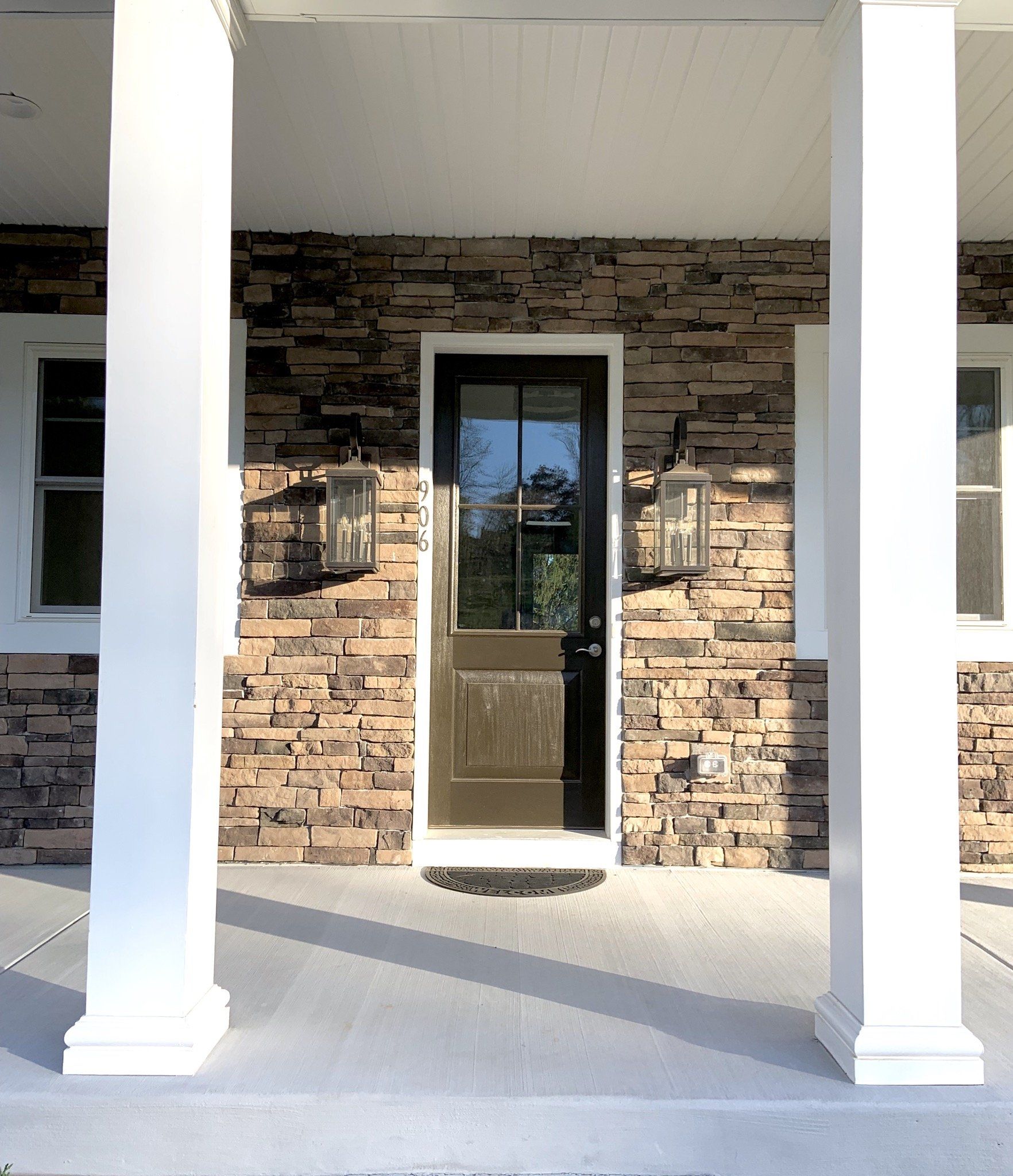 Front porch with white columns, brown door, and stone wall.