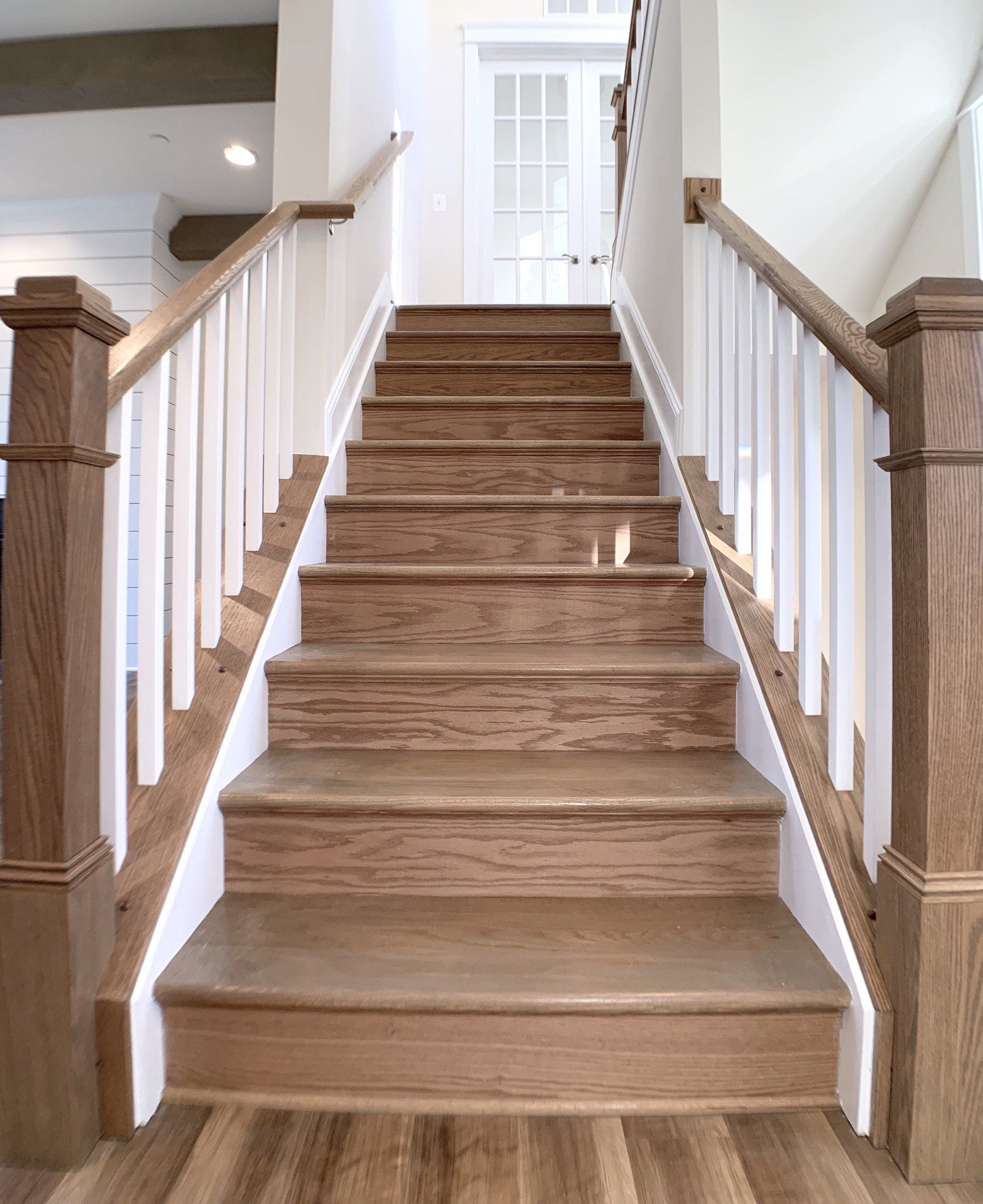 Wooden staircase with white railings and oak treads, leading up to a white door.