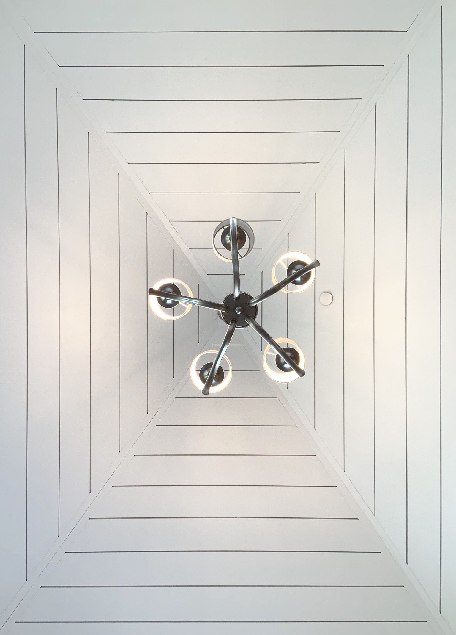 View looking up at a white ceiling with square recessed panels and a black chandelier with five glass globes.