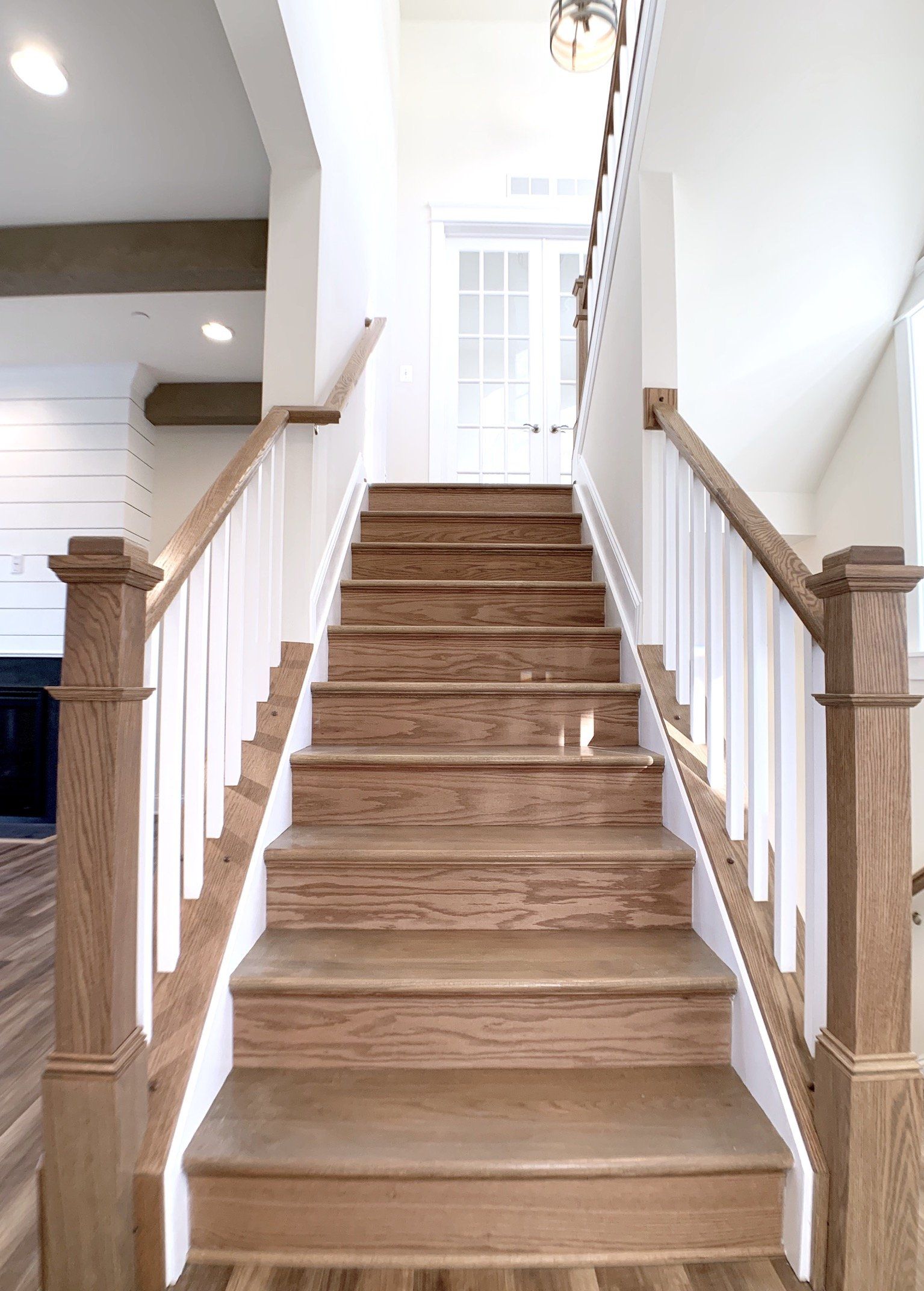 Wooden staircase with white railing leading to a doorway, bright, neutral-toned room.