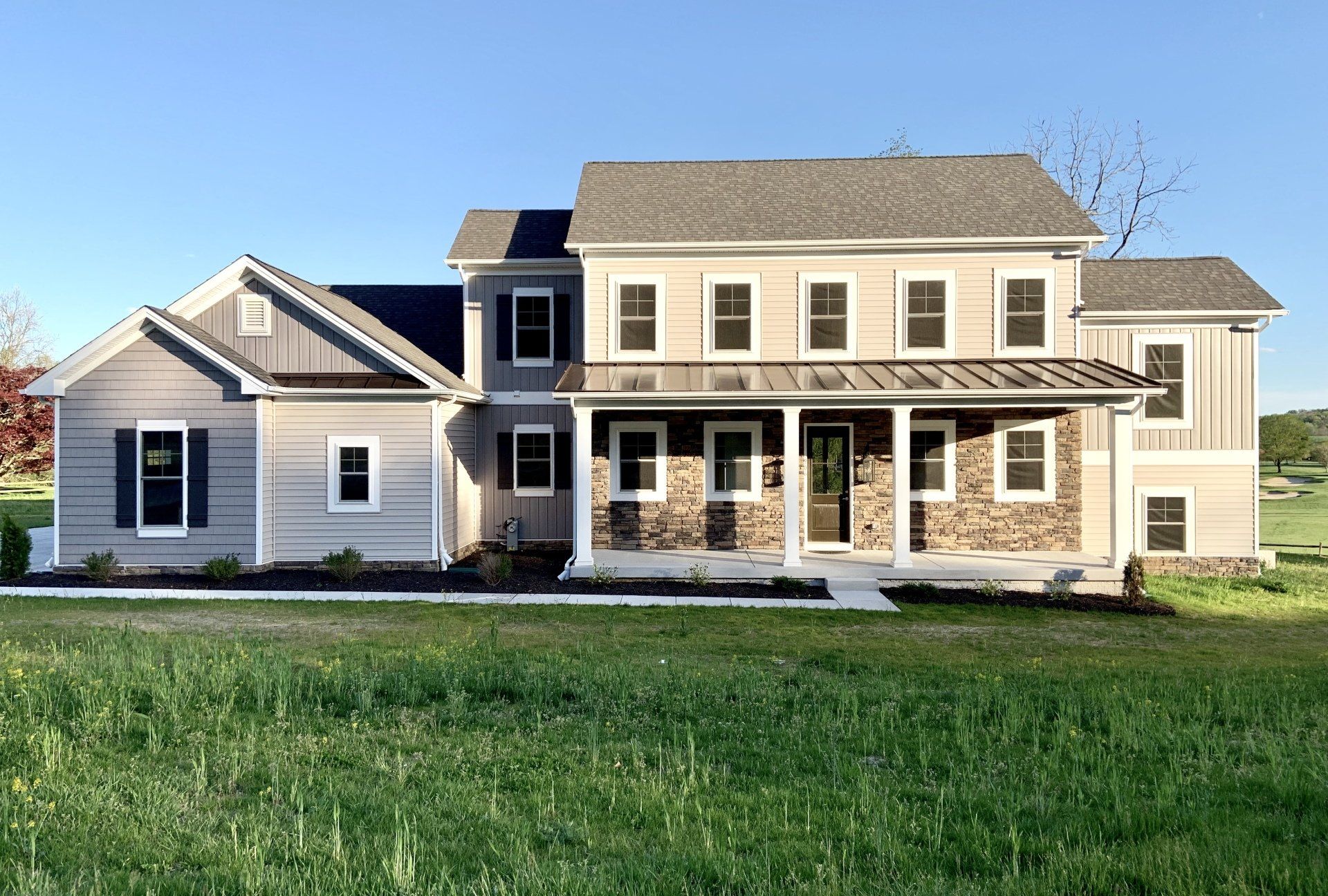 Two-story gray house with stone accents, front porch, and green lawn under a blue sky.