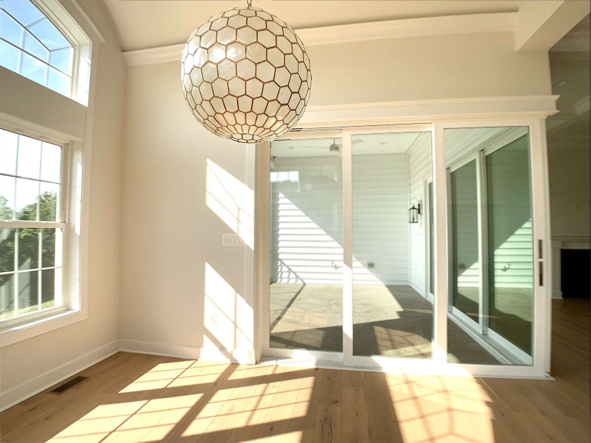 Bright white dining room with sliding glass doors, wood floors, and a geometric pendant light.