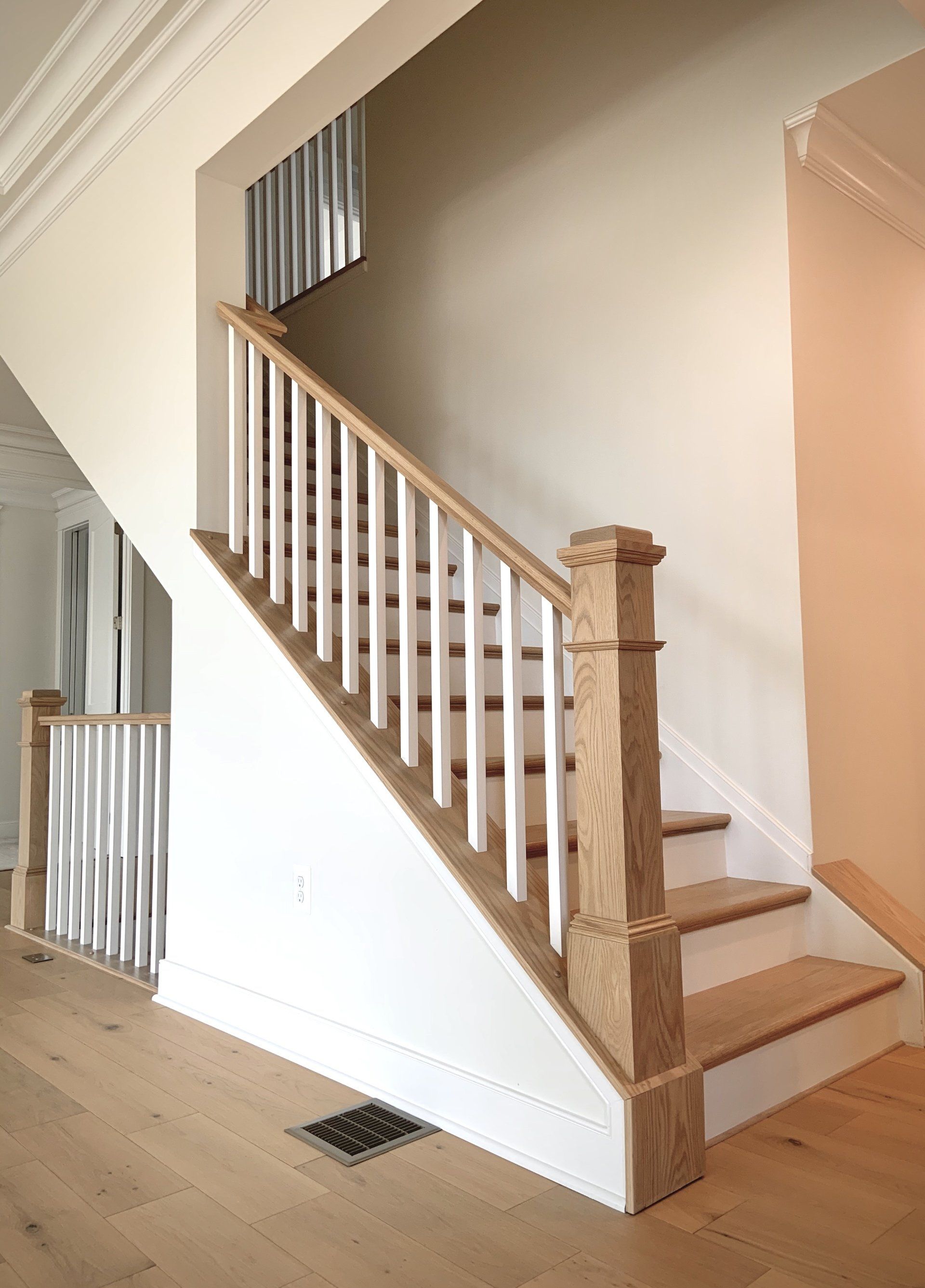 Staircase with light wood steps and railings, white spindles, and a wood newel post, indoors.