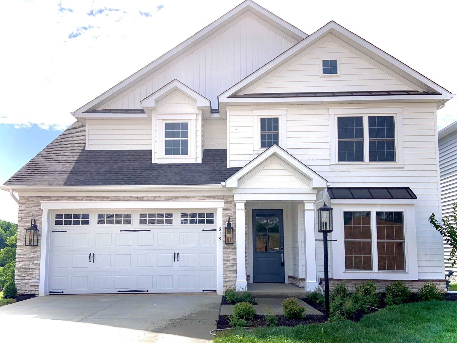 White two-story house with stone accents, blue door, and black roof and garage door.