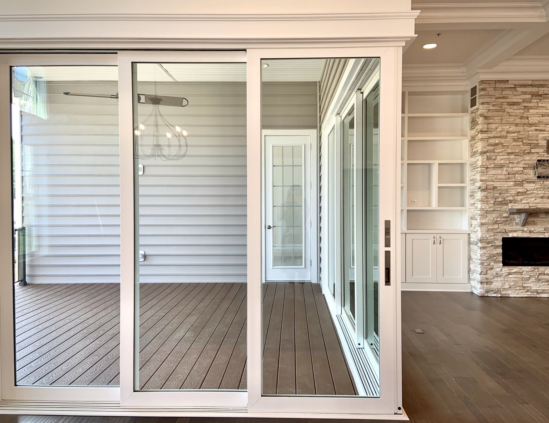 White sliding glass doors open to a deck, light wood floors, and a gray-walled room; to the right, a fireplace.