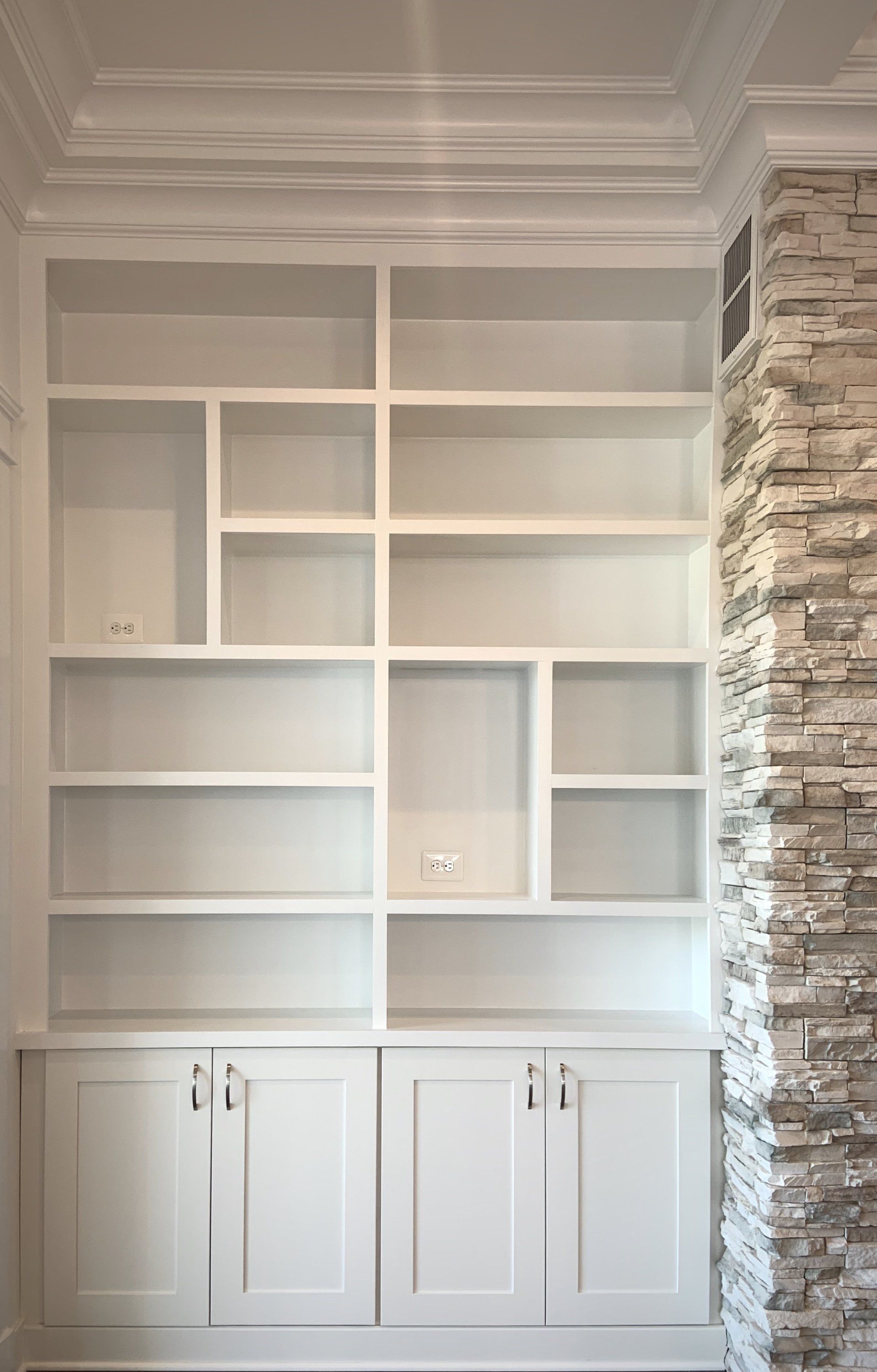 White built-in bookcase with shelves and lower cabinets; next to a stone wall.