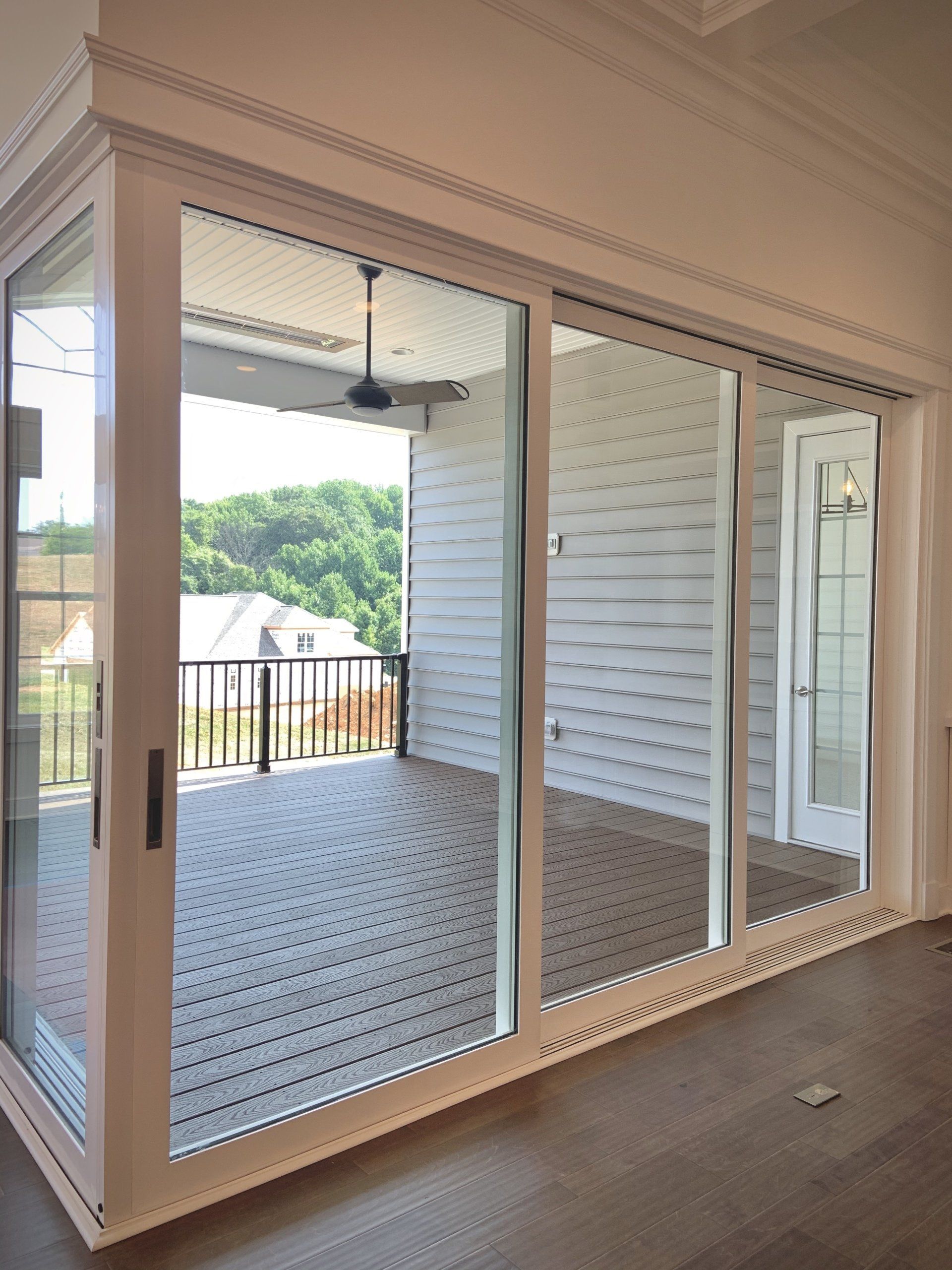 Sliding glass doors open to a deck with a ceiling fan, overlooking a wooded area.