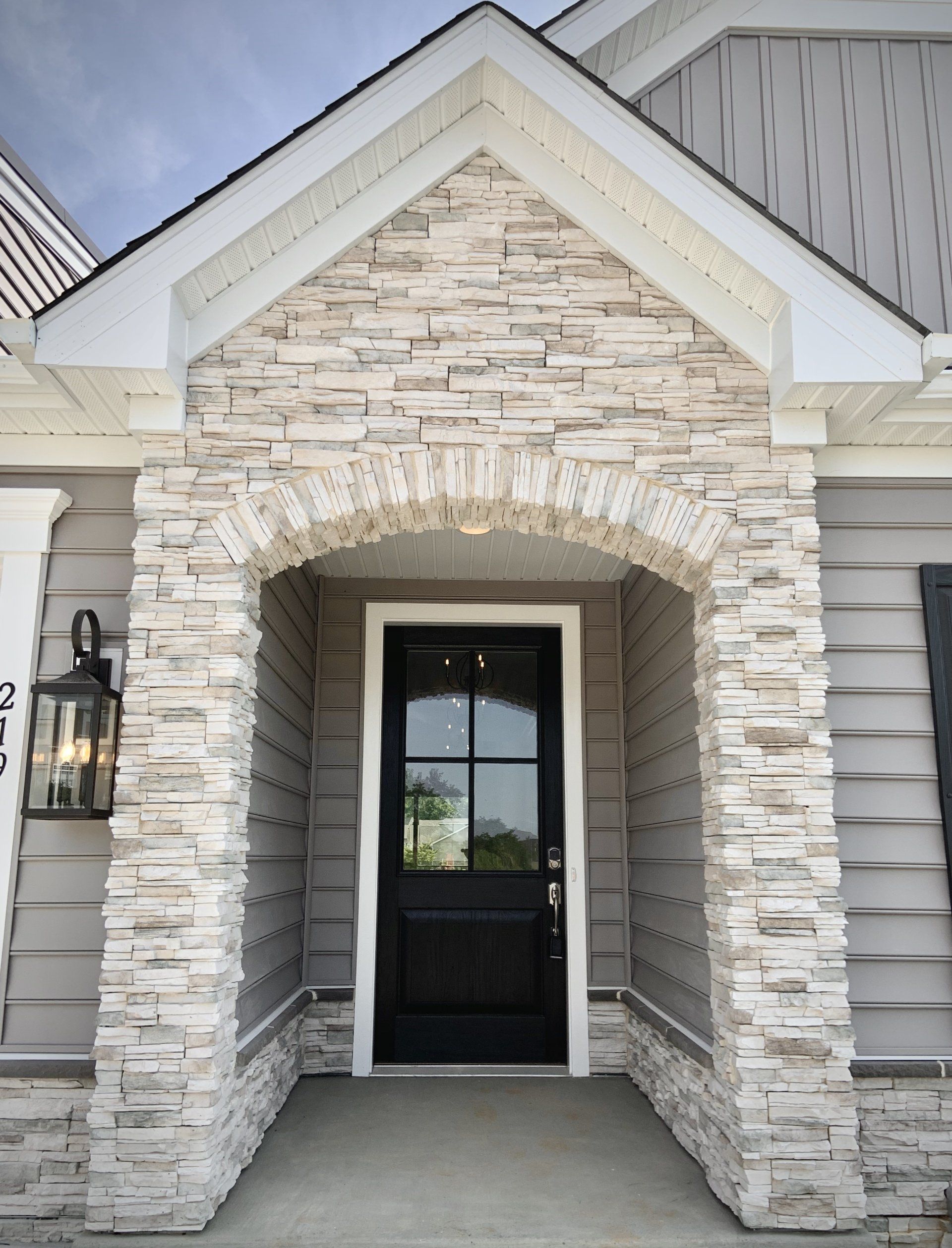 Stone-arched doorway entrance with black door, gray siding, and white trim.