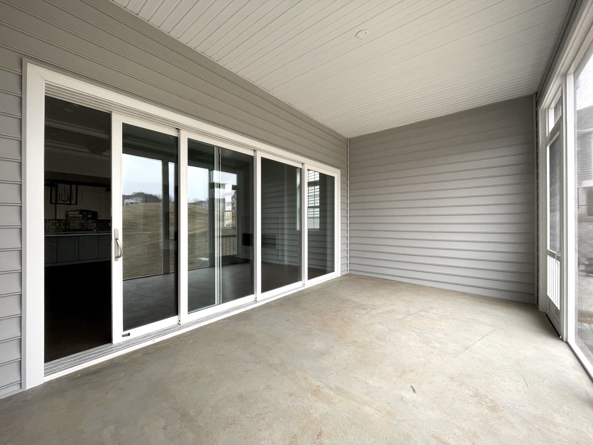 Sunroom with gray siding and sliding glass doors; concrete floor.