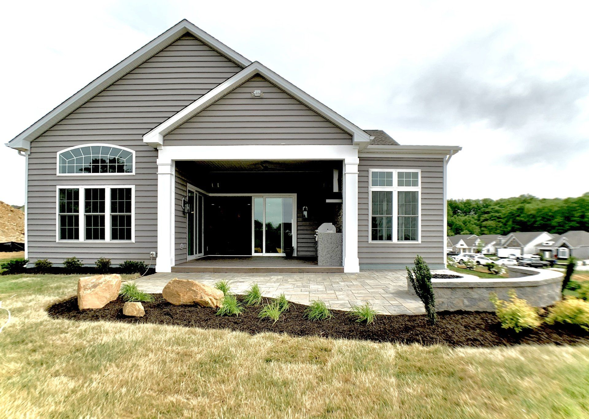 Gray house with patio, sliding doors, and a stone fire pit in a backyard on a cloudy day.