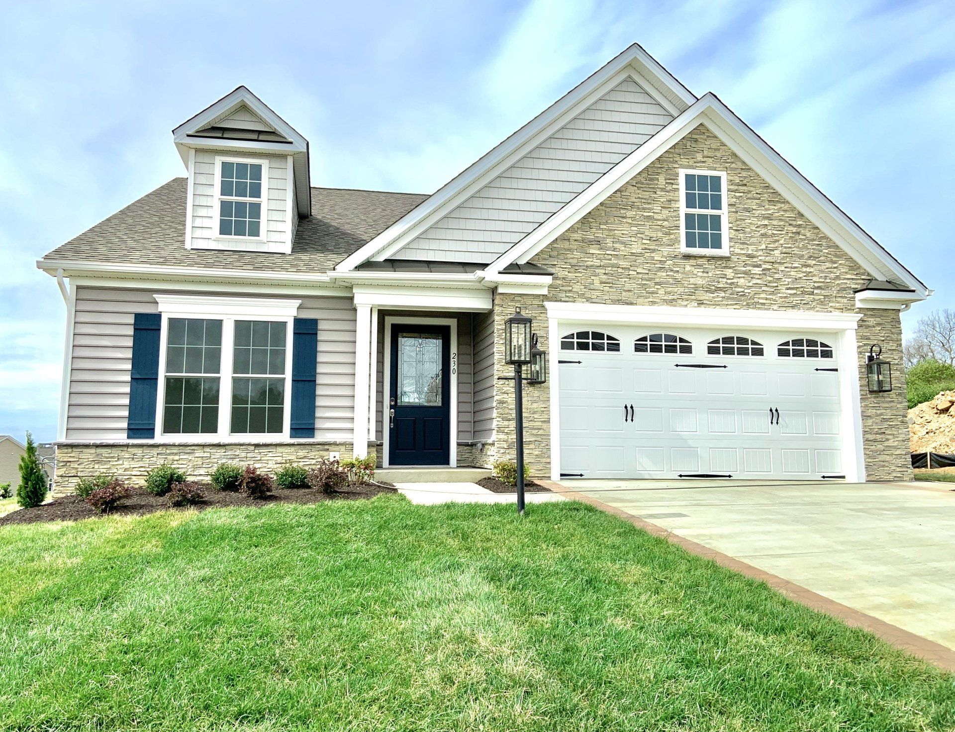Tan and gray house with blue shutters and a white garage door. Green lawn.
