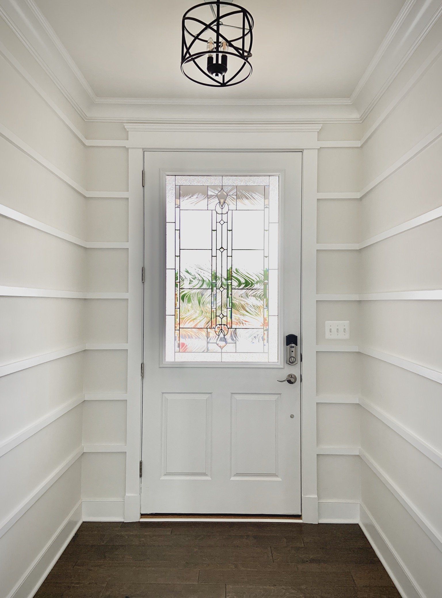 White entryway with white door, trim and paneling; black light fixture; door has window.
