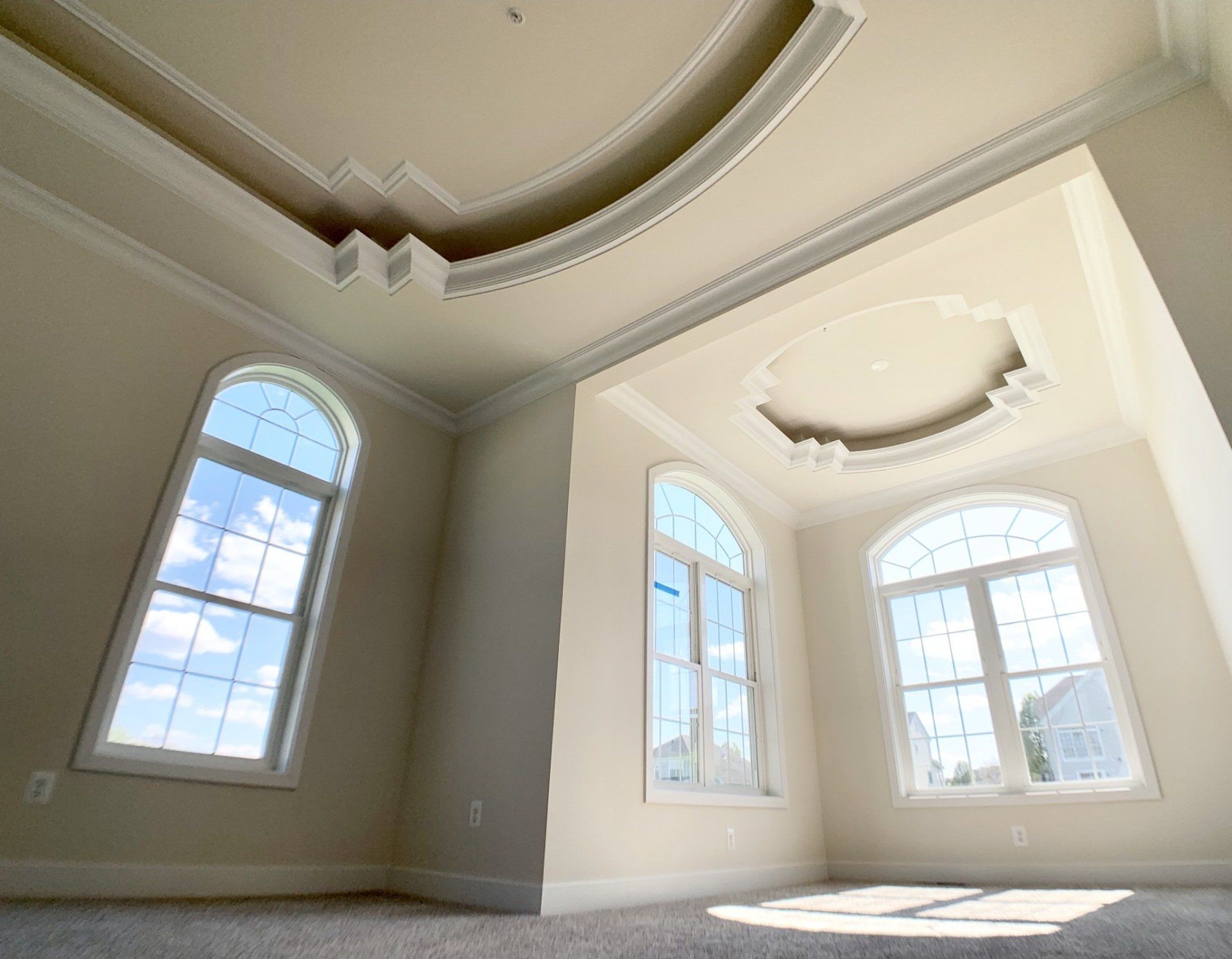 Empty room with arched windows, ornate ceiling molding, and beige walls.