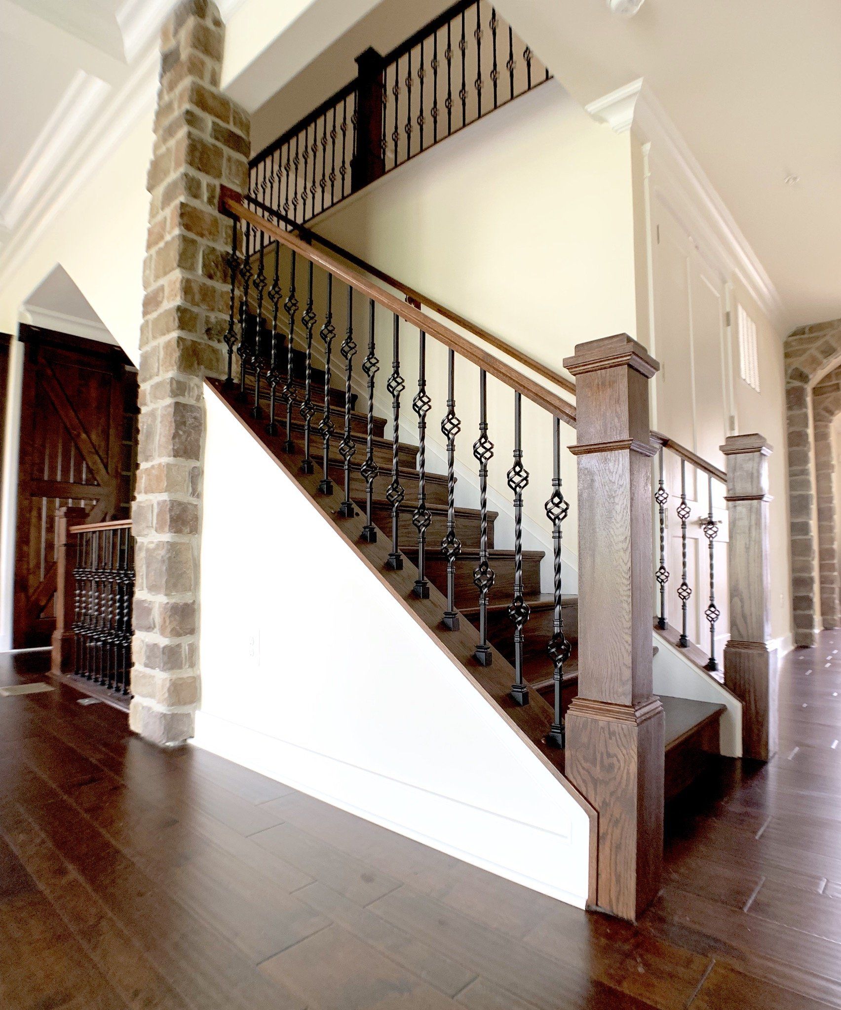 Wooden staircase with wrought iron balusters, stone accents, and dark hardwood flooring.