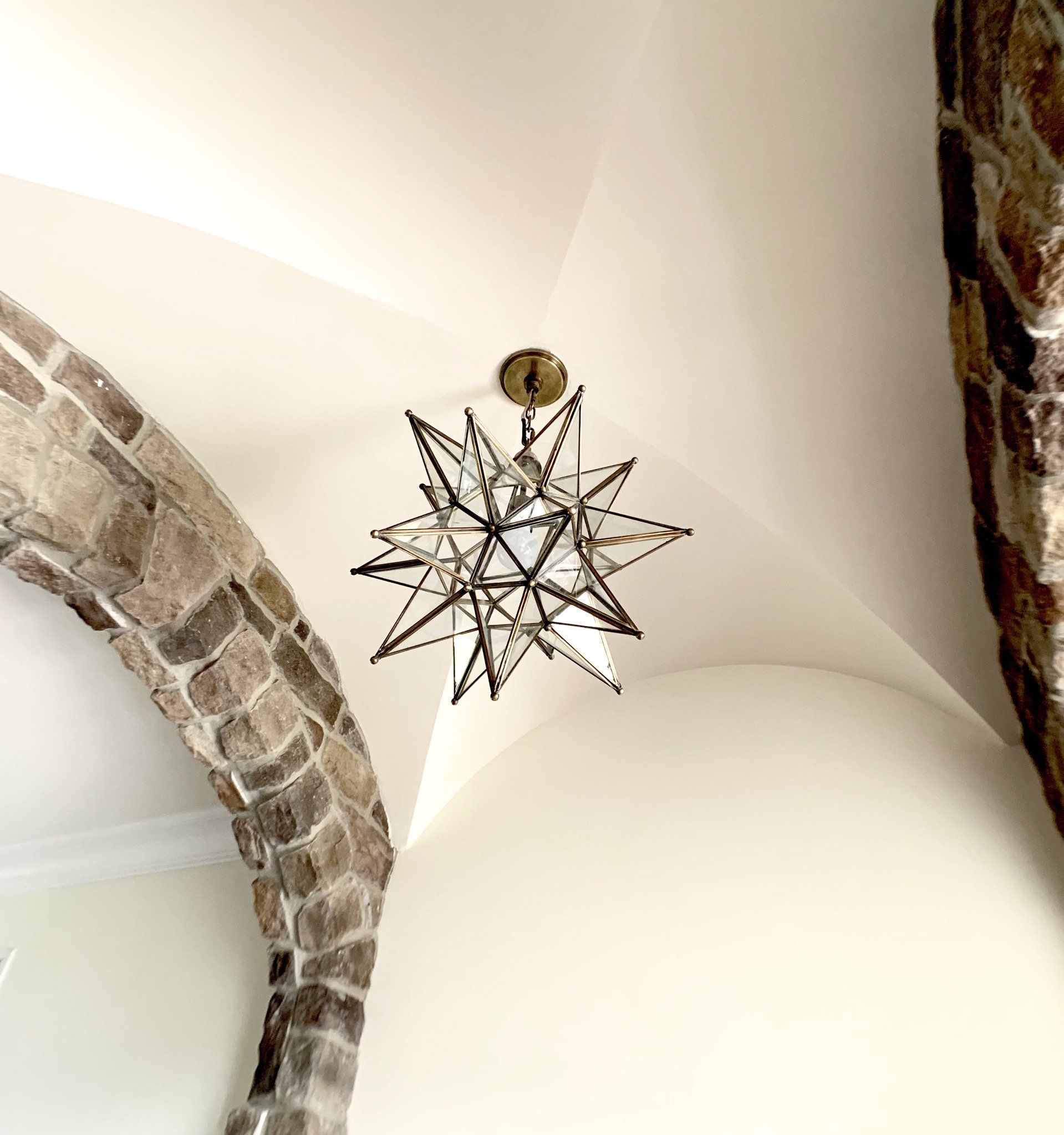 Star-shaped chandelier hangs from a curved, white ceiling, near stone archway and wall.