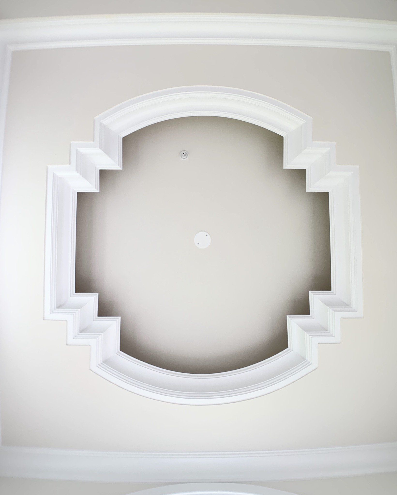 Ornate white ceiling medallion with a recessed center, set against a light beige ceiling.