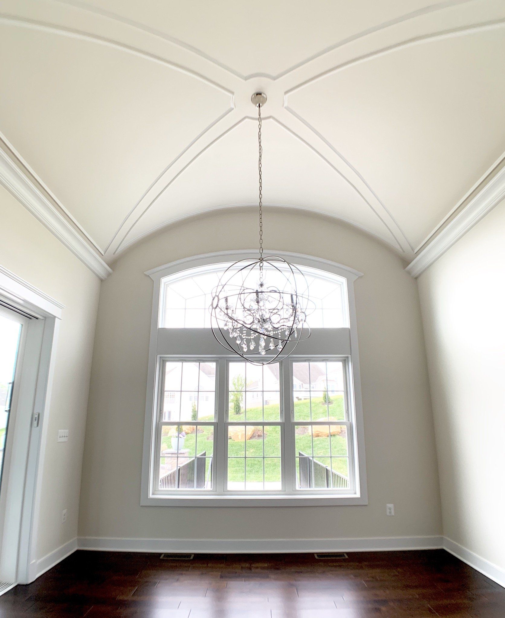 High-ceilinged dining room with dark wood floor, large window, and ornate chandelier.