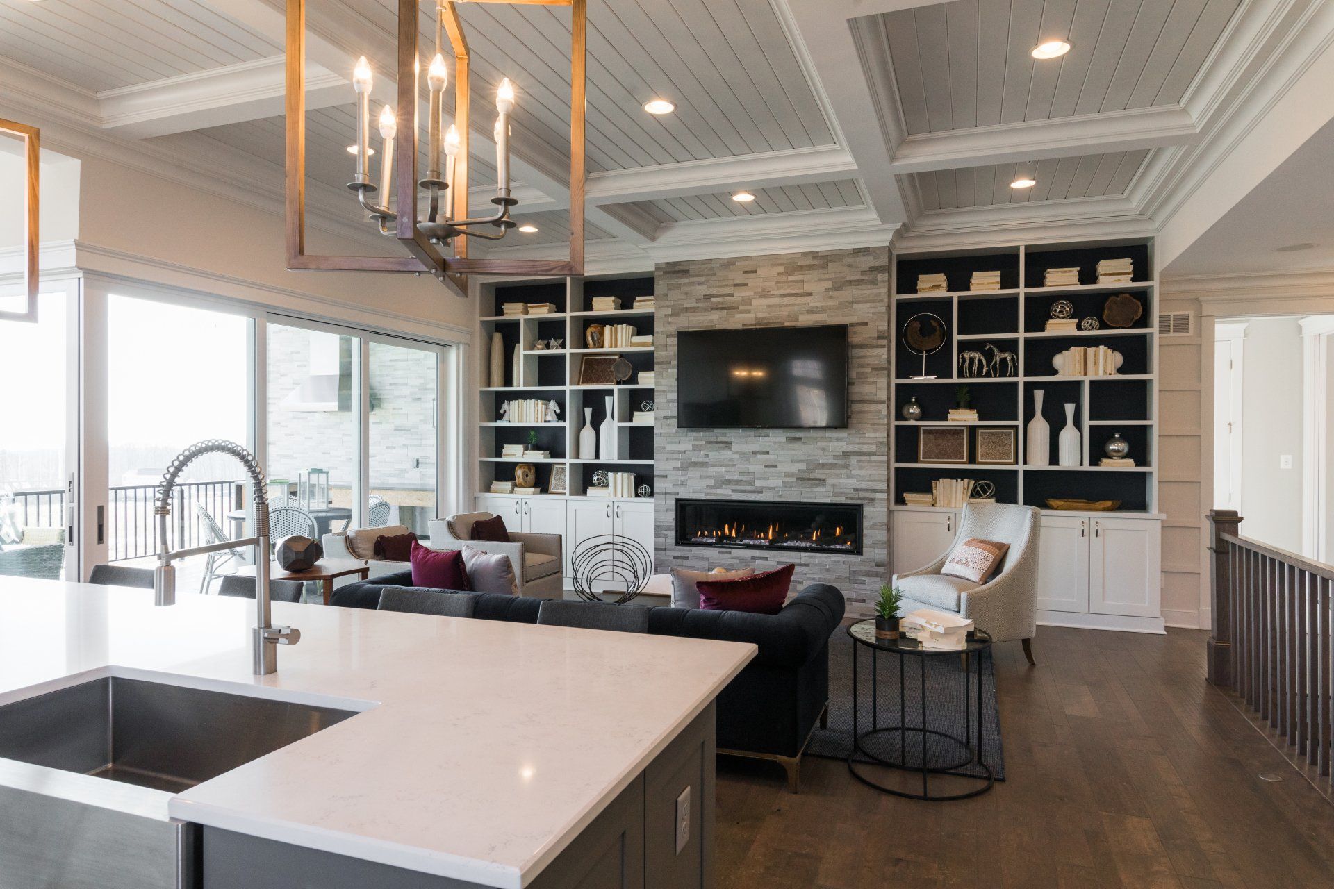 Modern living room with fireplace, built-in shelves, and kitchen island, with large windows overlooking a balcony.