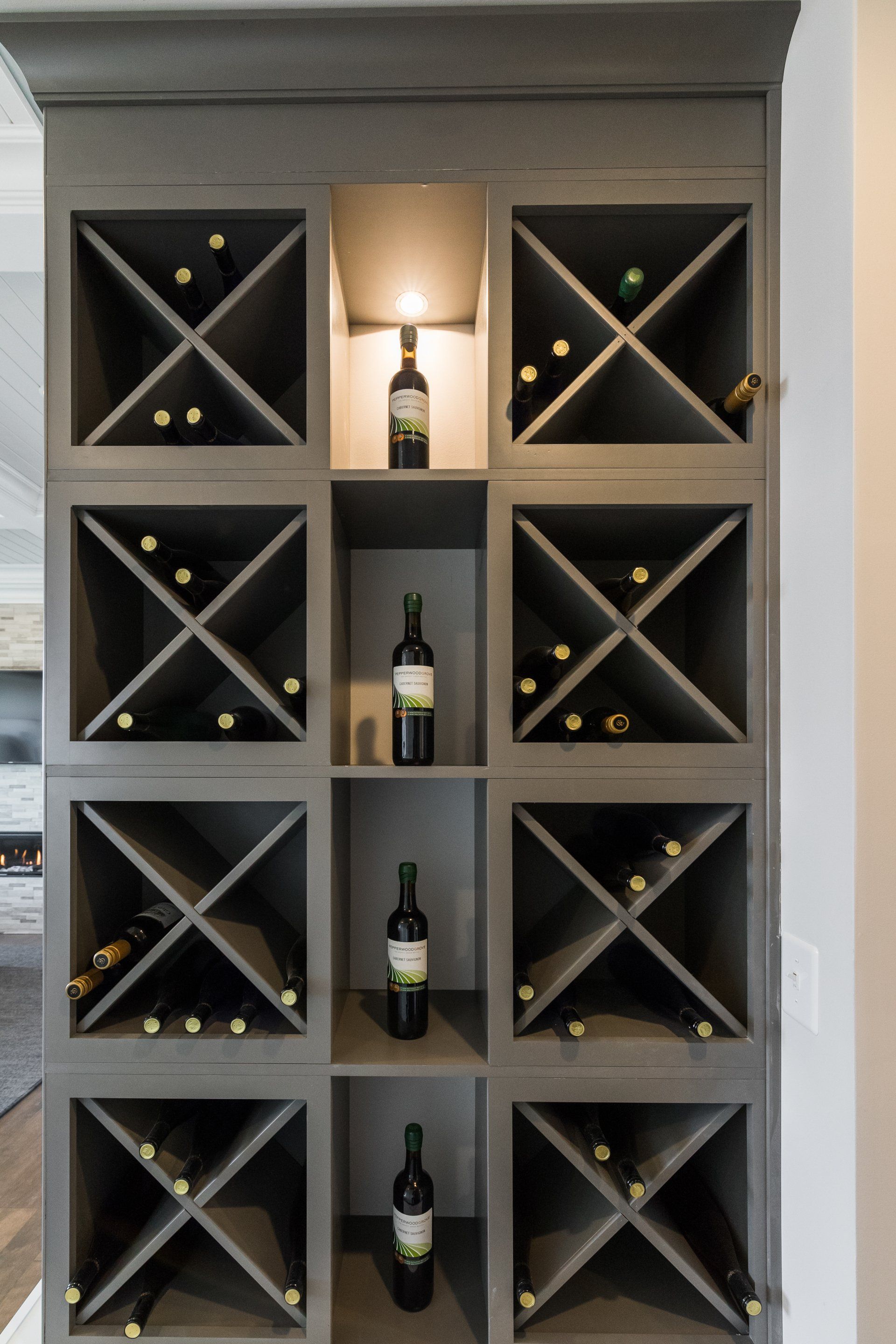 Gray built-in wine rack with multiple bottle storage compartments, some with bottles, in a home.