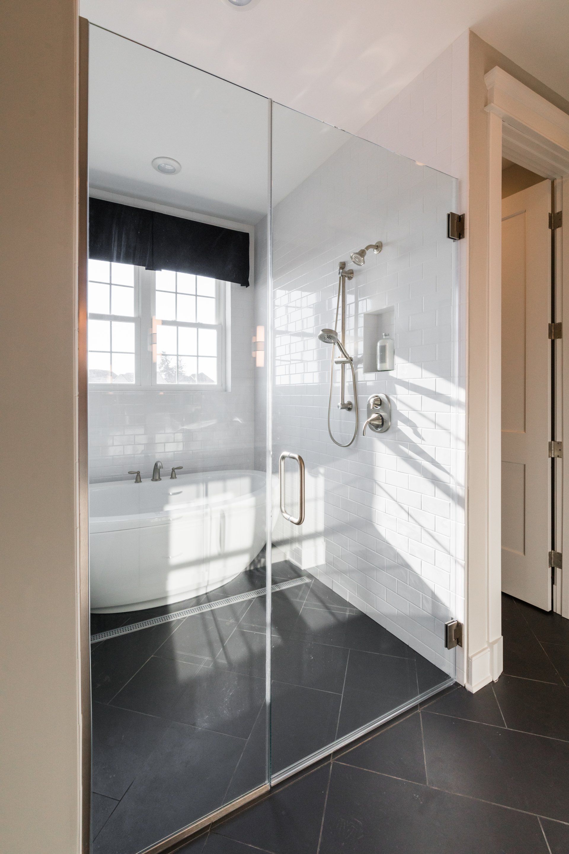 Modern bathroom with glass shower, tub, black floor, and white walls.