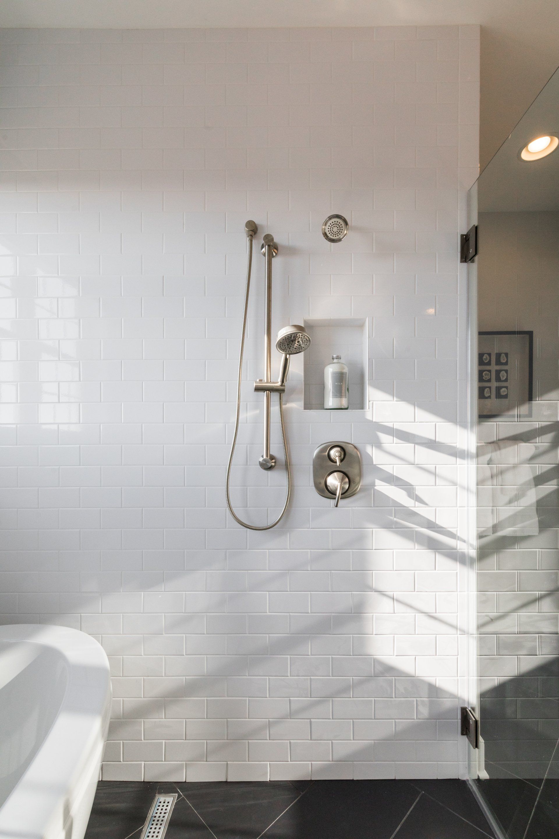 White tiled shower with silver fixtures, a built-in shelf, and a glass door.