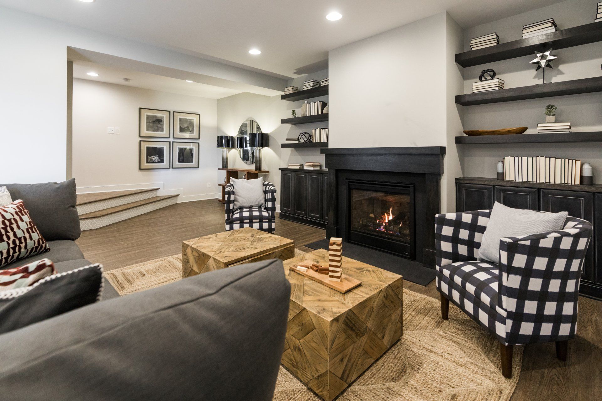 Cozy basement living room with fireplace, sofa, plaid armchair, and wooden shelves with decor.