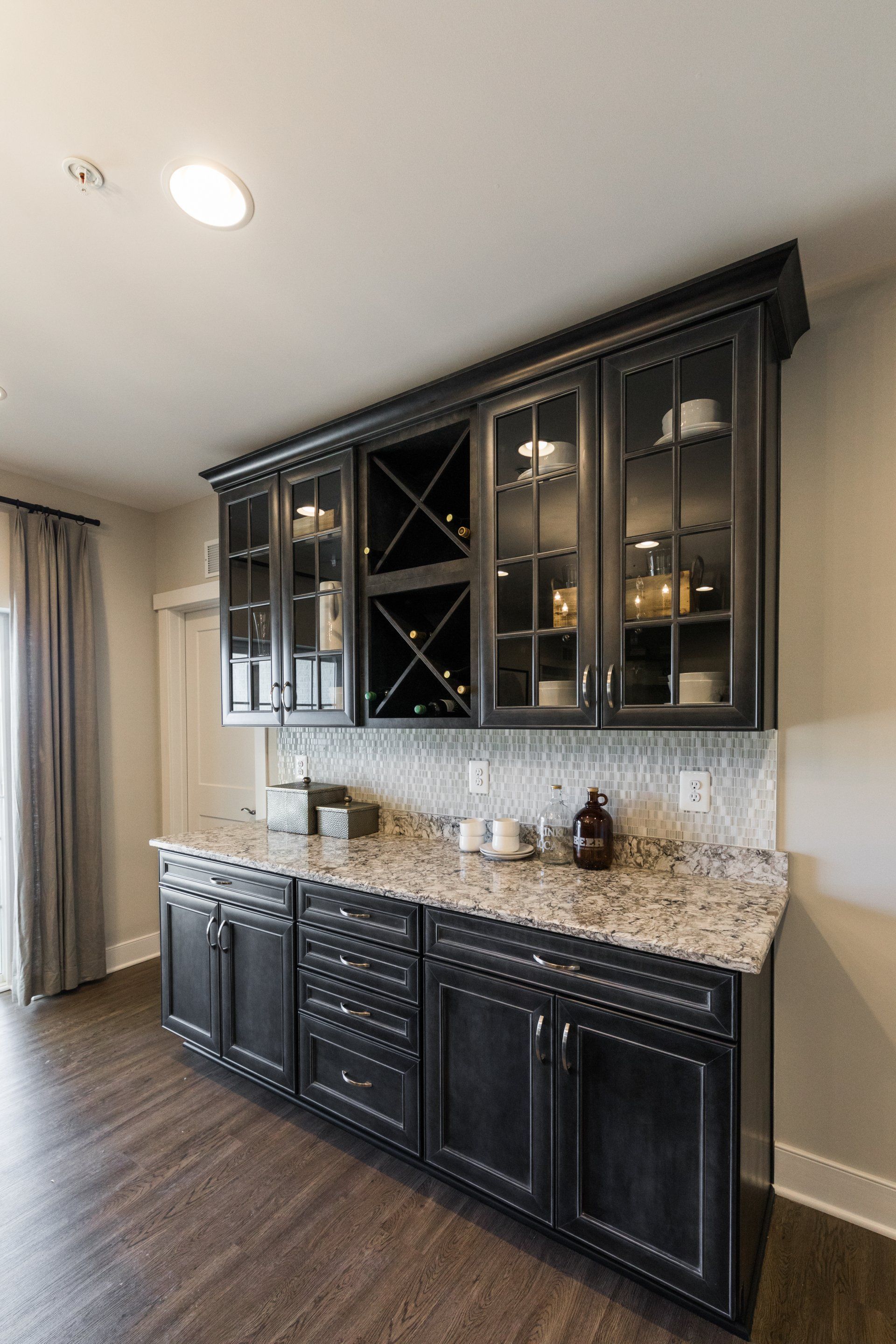 Dark grey built-in bar with wine rack, cabinets, granite countertop, and glass-door uppers.