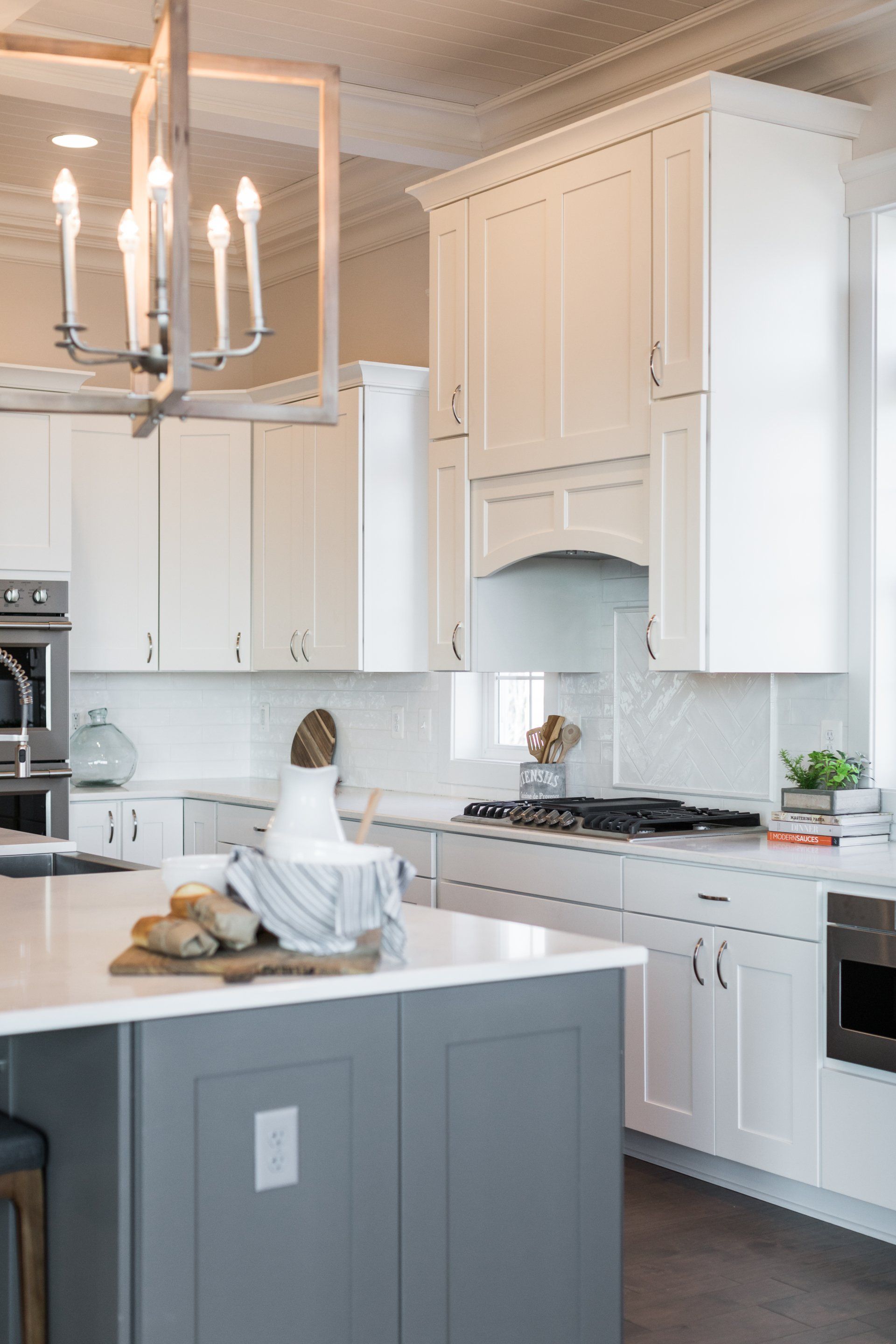 Modern kitchen with white cabinets, gray island, stainless steel appliances, and a chandelier.