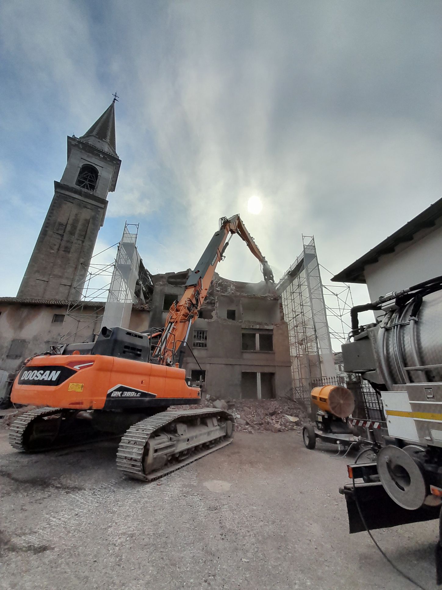 Un grande escavatore arancione sta demolendo un edificio.