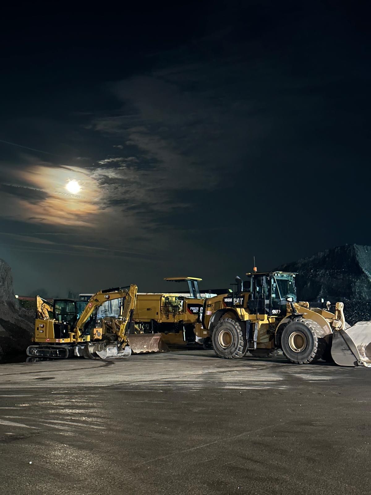Di notte un gruppo di veicoli da cantiere è parcheggiato in un parcheggio.