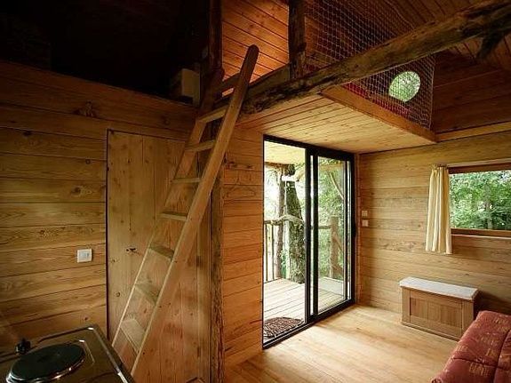 Houten interieur van een blokhut met een mezzanine, een ladder en een glazen schuifdeur naar een balkon.