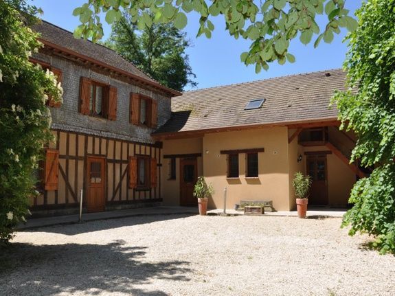 Exterieurbeeld van een gebouw met twee verdiepingen, een lichtgekleurde gevel, houten luiken en een binnenplaats.