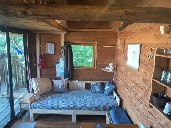 Houten interieur van een blokhut met een mezzanine, een ladder en een glazen schuifdeur naar een balkon.