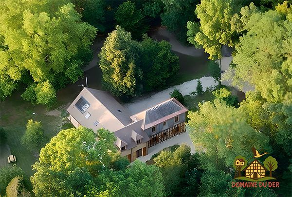Luchtfoto van een lichtbruin huis met een donker dak, omgeven door groene bomen.