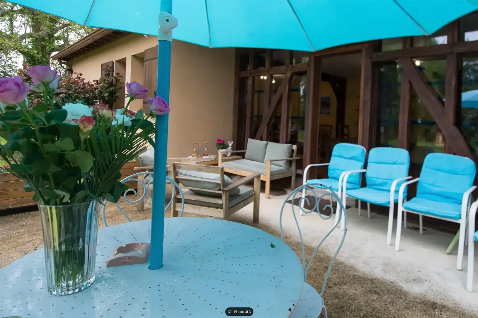 Terras met blauwe parasol, stoelen en tafel. Bloemen in een vaas. Zonlicht, buitenomgeving.