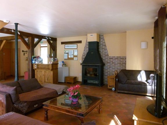 Ruime woonkamer met open haard, bruine banken, houten balken en een salontafel.