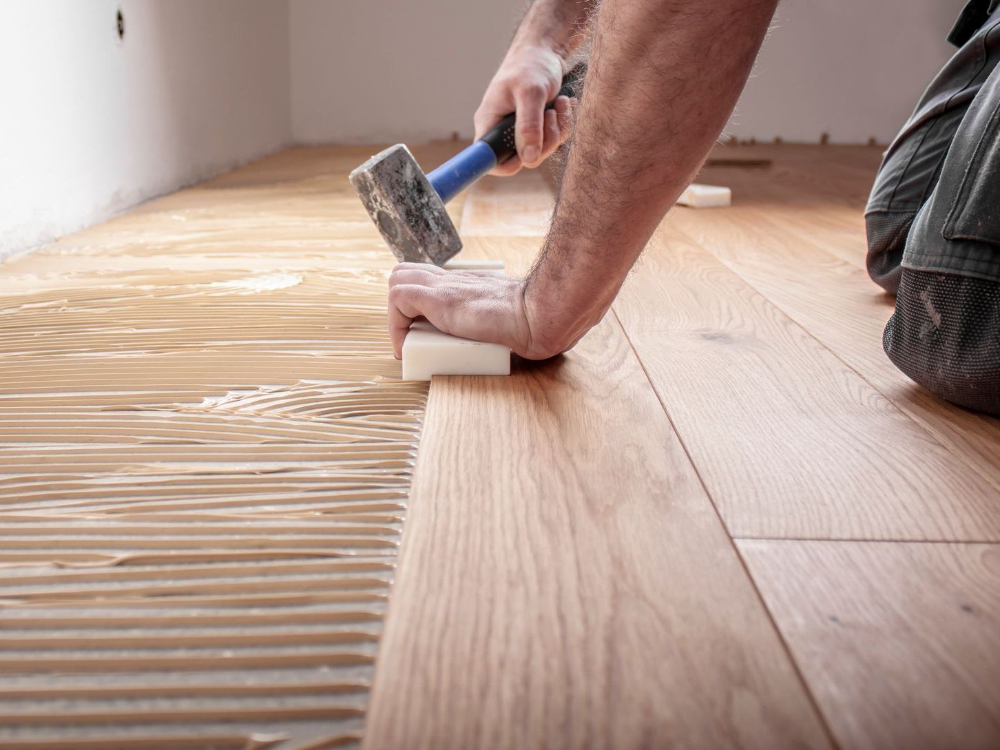 A man is using a hammer to install a wooden floor.