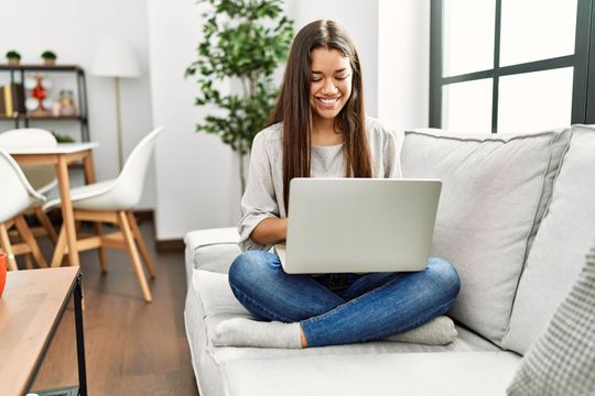 A woman is sitting on a couch using a laptop computer.