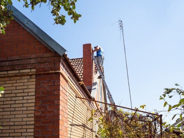Worker on a ladder repairing a brick building roof edge