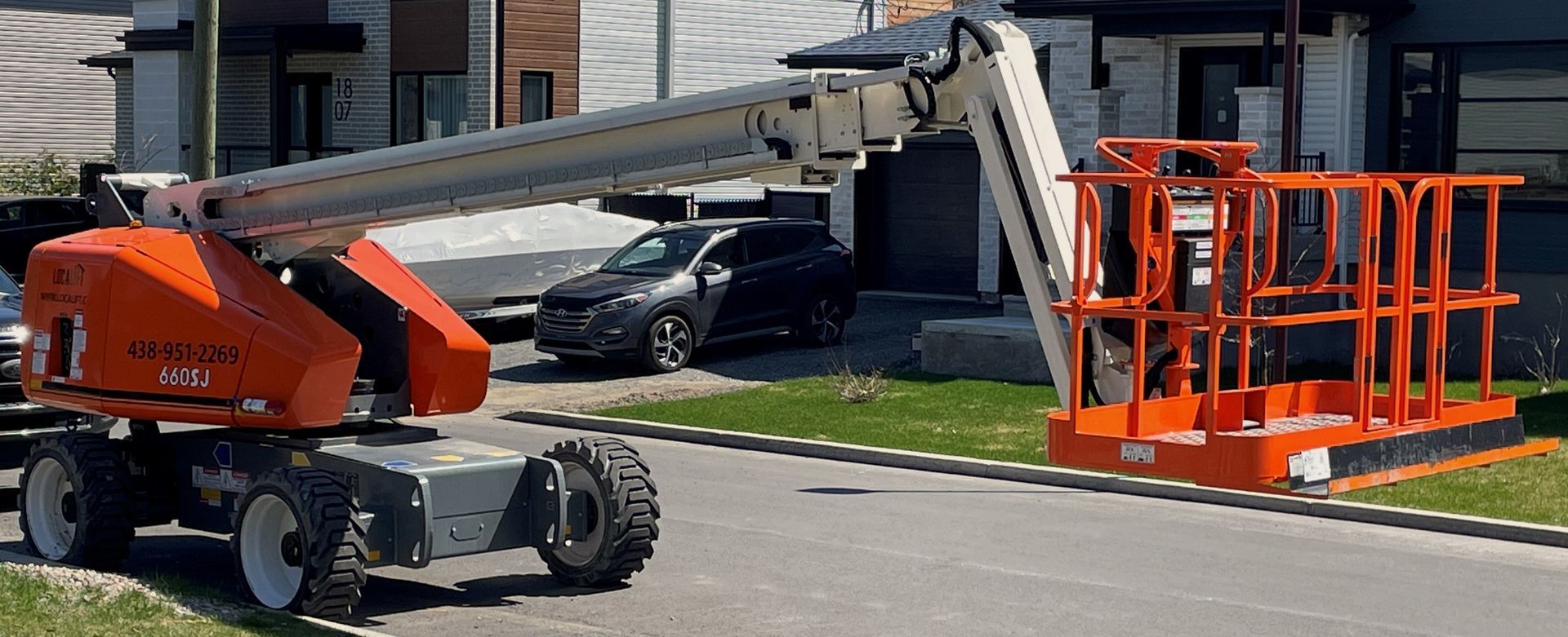 Une grue est garée sur le bord de la route devant une maison.