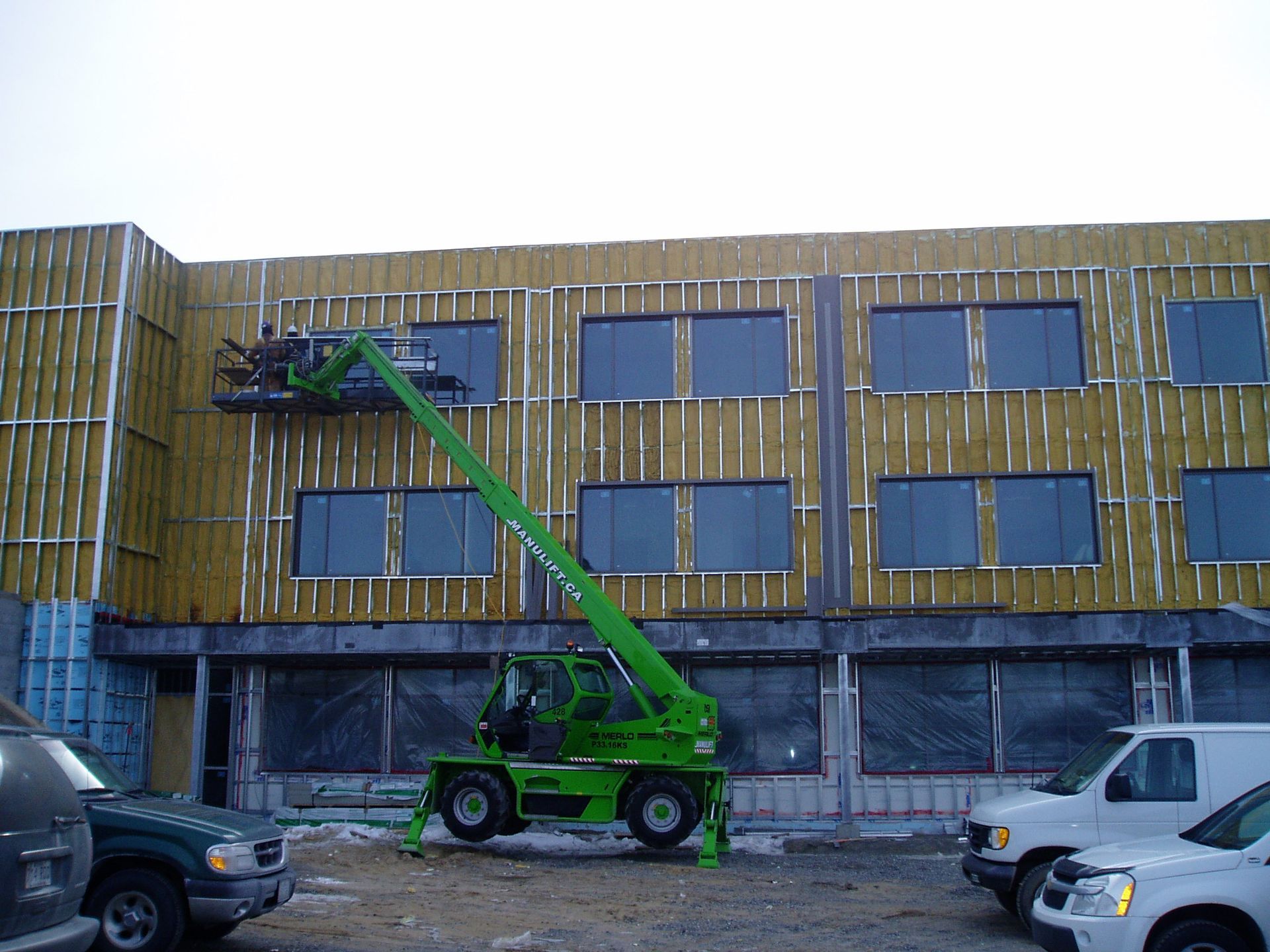 Une grue verte travaille sur le côté d'un bâtiment.