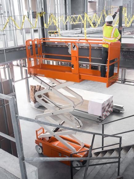 Un homme travaille sur une nacelle élévatrice à ciseaux sur un chantier de construction.