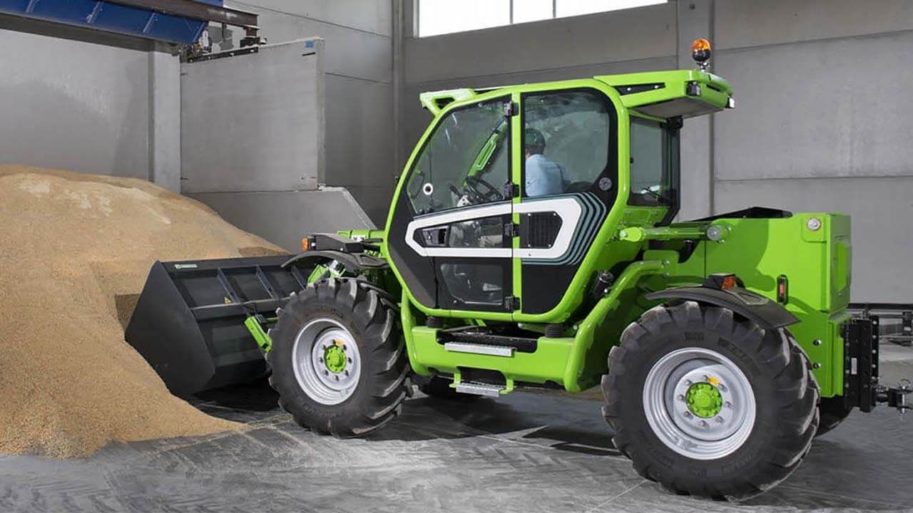 Un chariot élévateur vert charge du grain dans un entrepôt.