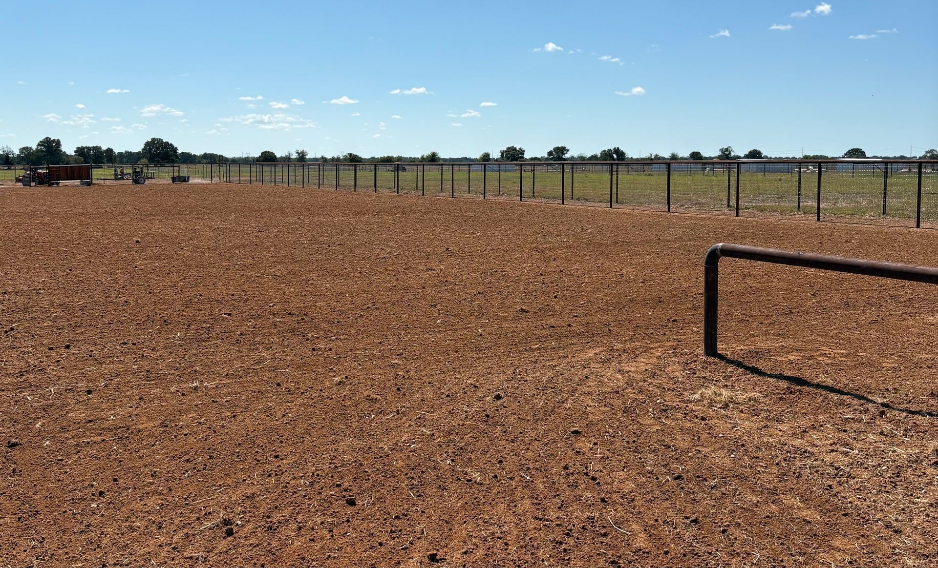 Brown dirt field, black fence, blue sky, rural landscape.