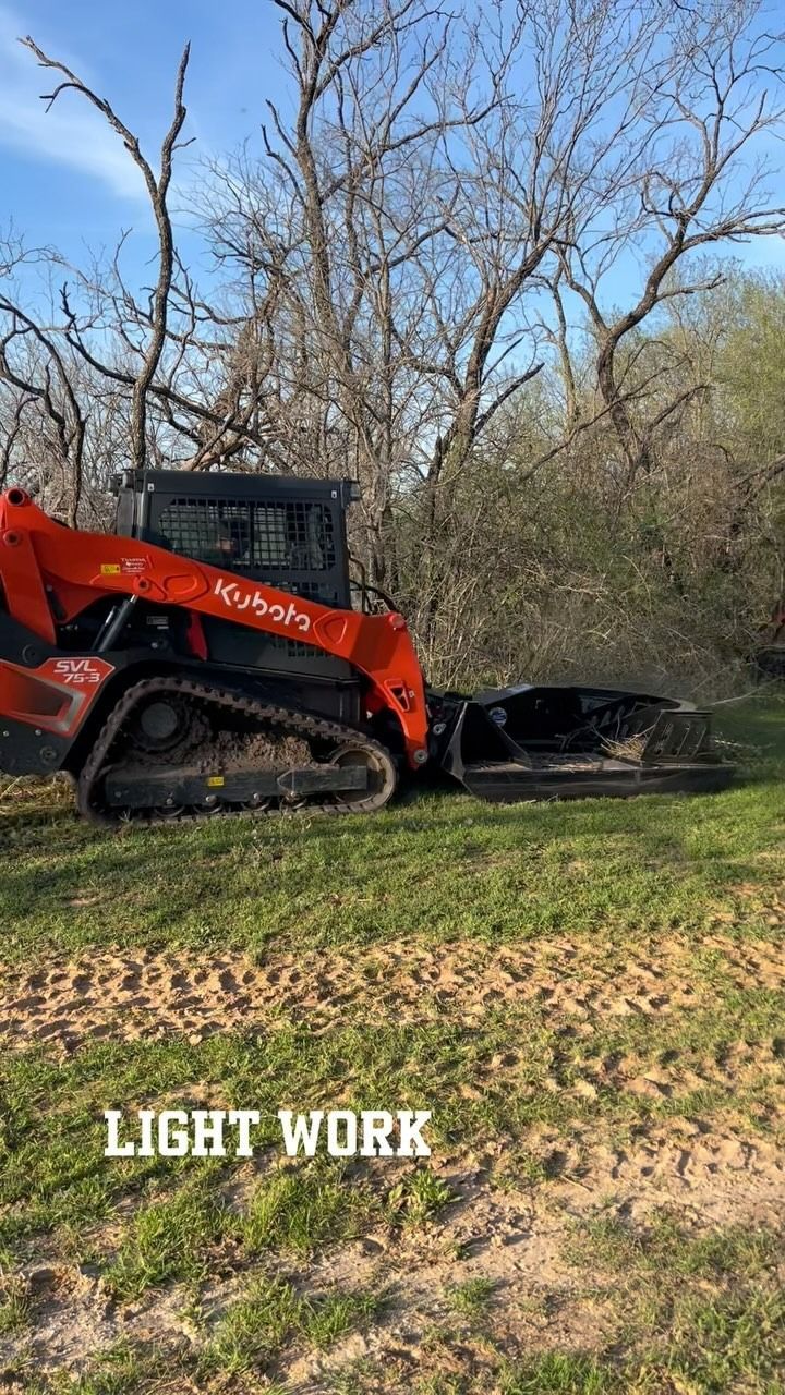 Orange Kubota skid steer clearing brush in grassy area.