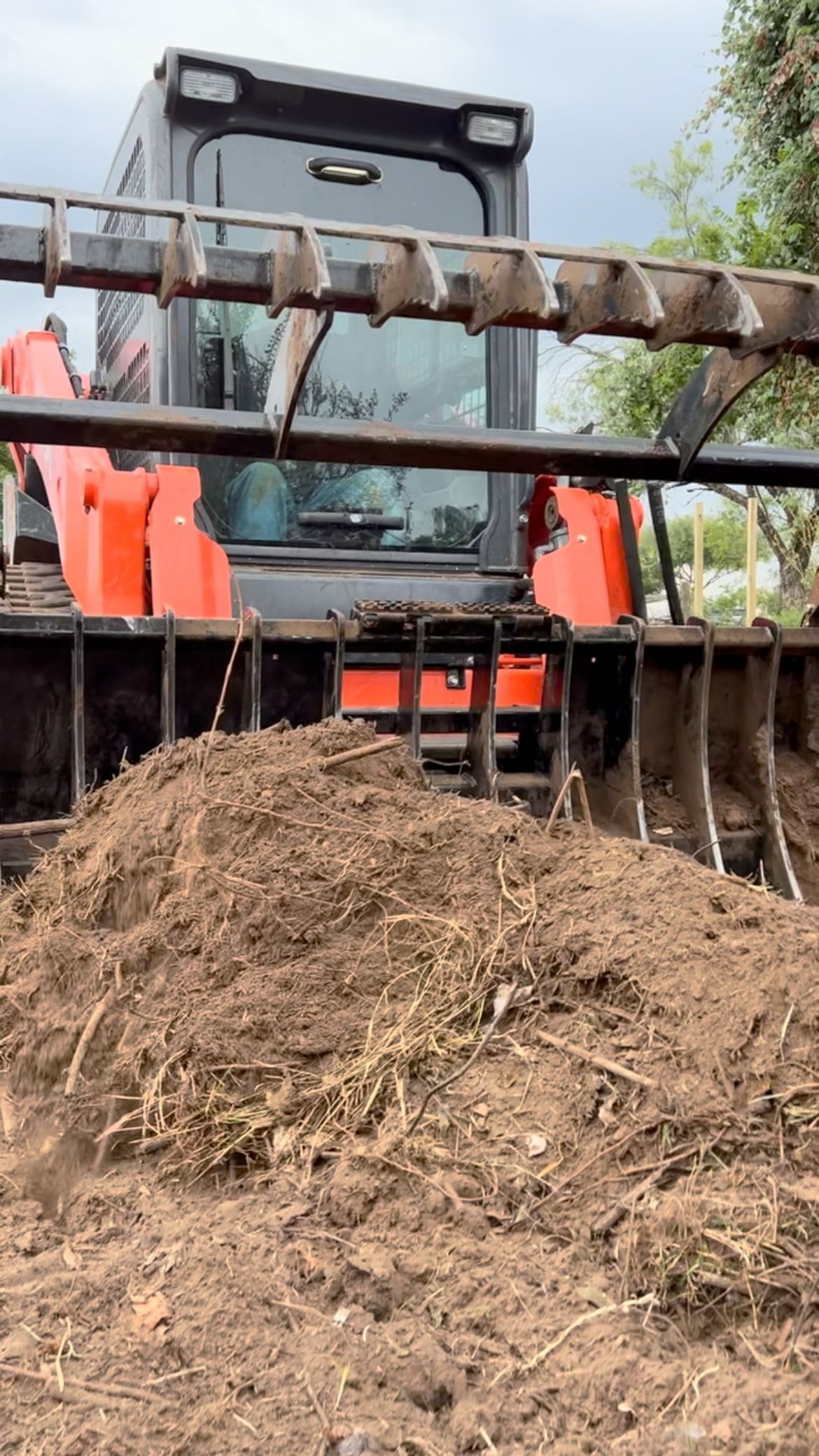 Skid steer with grapple bucket holding a pile of brown mulch.